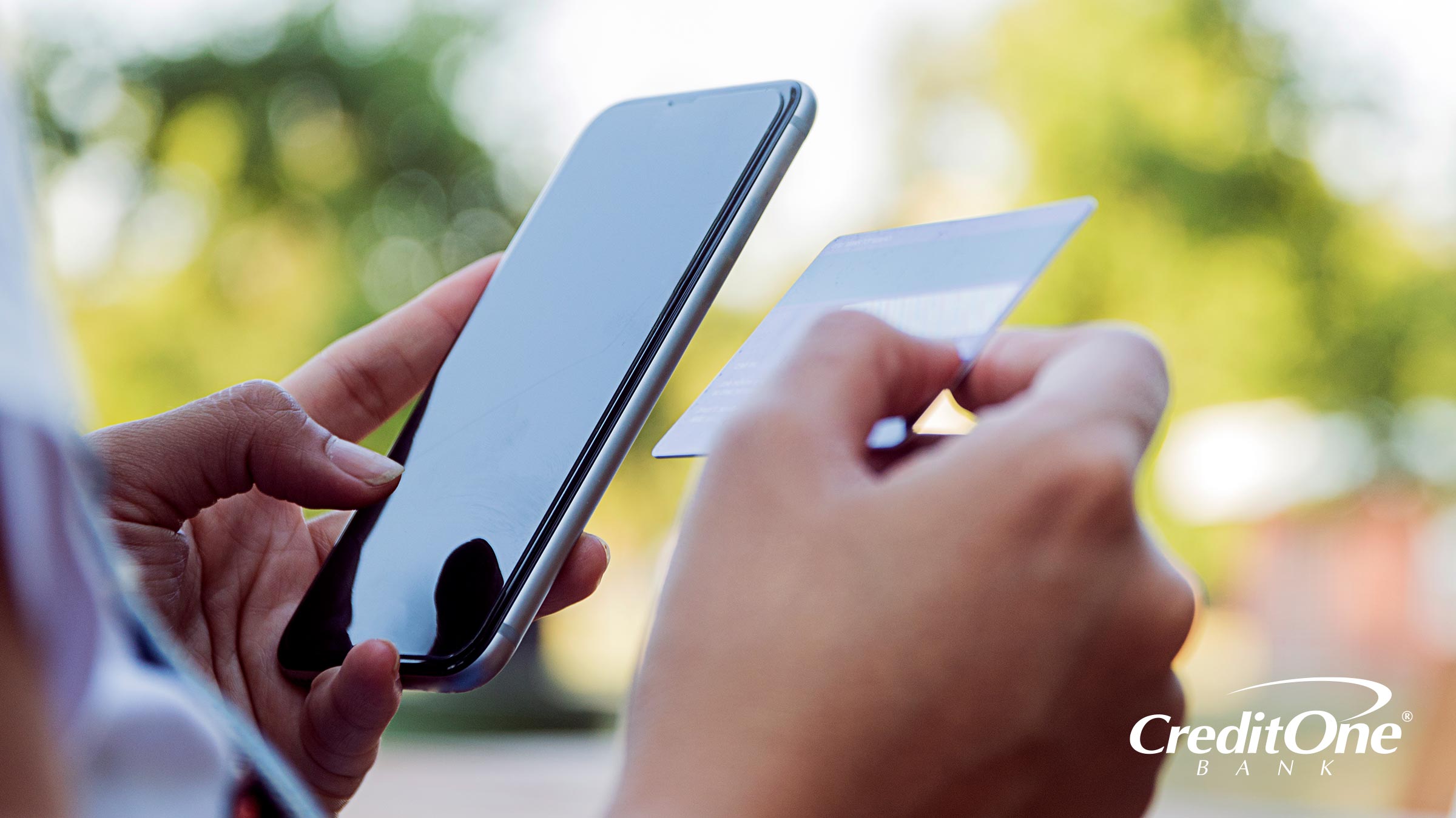 A person’s hand holds a phone while the other hand holds a credit card. They may be trying to check whether or not the credit card is active.