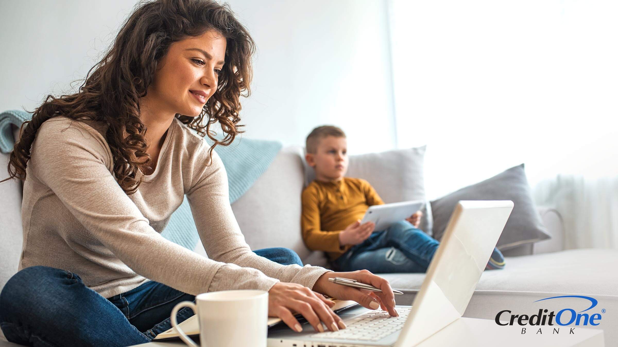 Mother smiling while working on finances with kid playing on tablet.