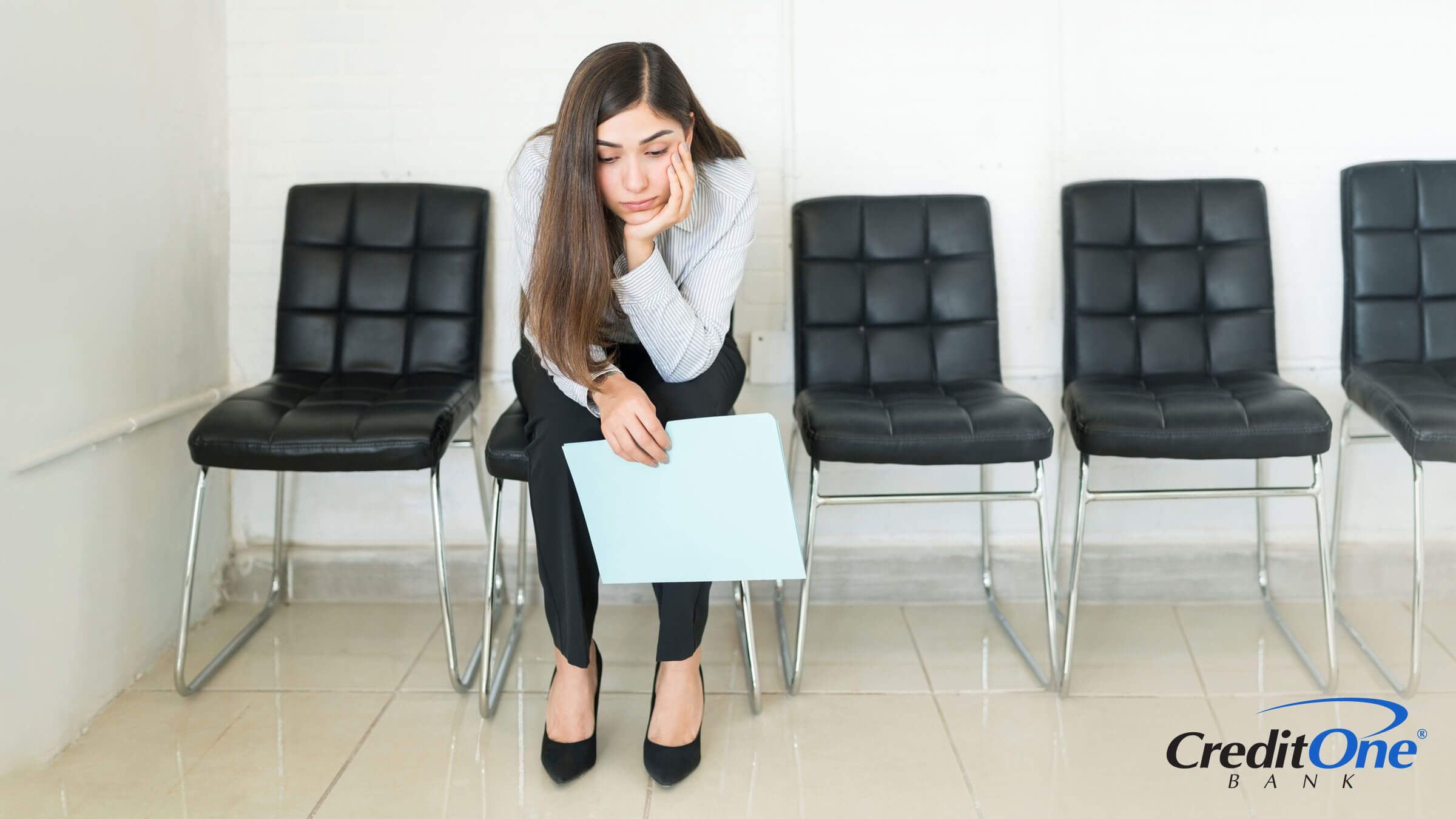 A young woman waits for her turn at a job interview, holding a folder as she looks thoughtfully at the floor, perhaps wondering if she can get a credit card to help make ends meet.