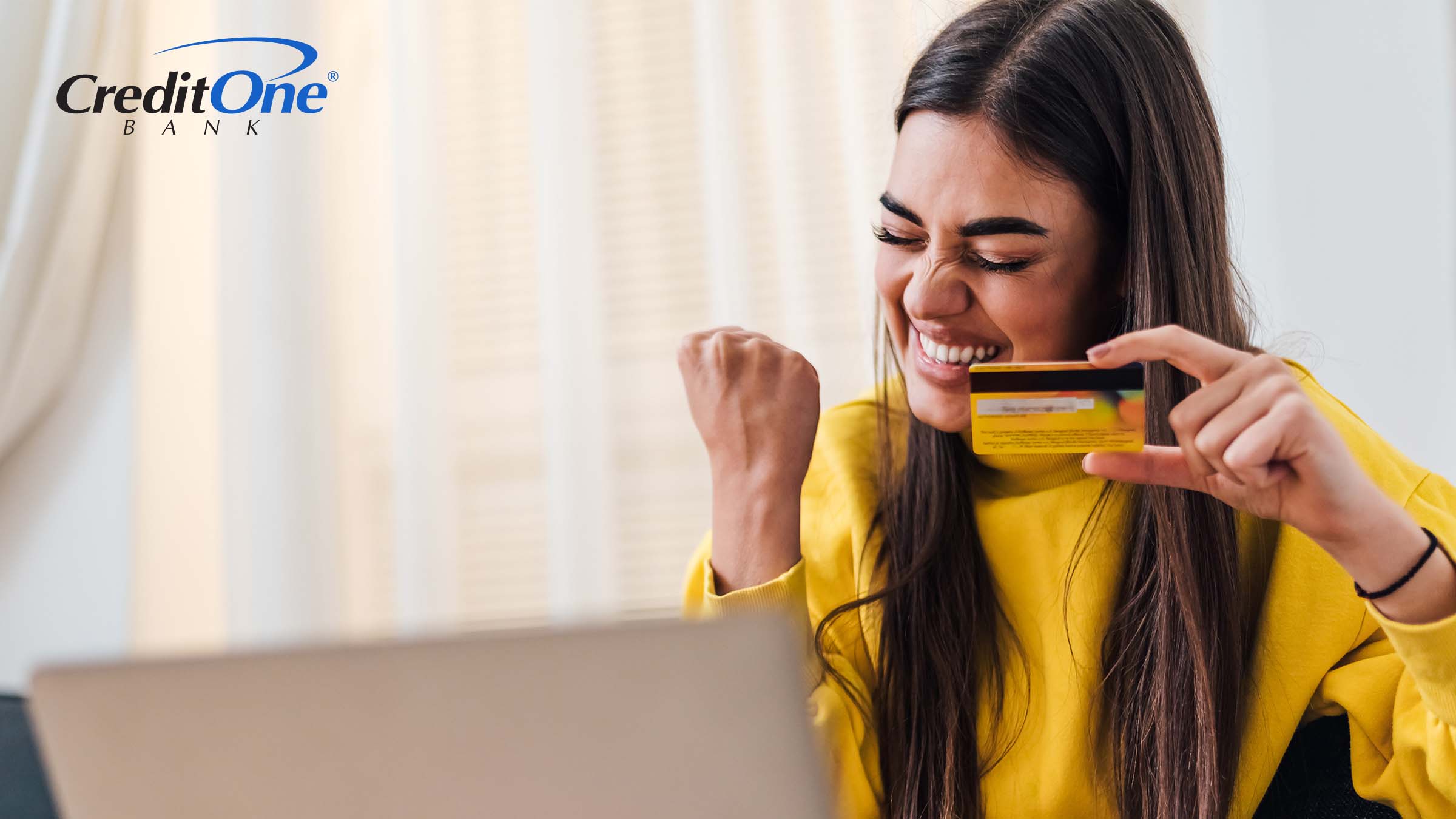 A young woman raises her fist in celebration while holding up her credit card, as if she’s pleased with her starting credit score.