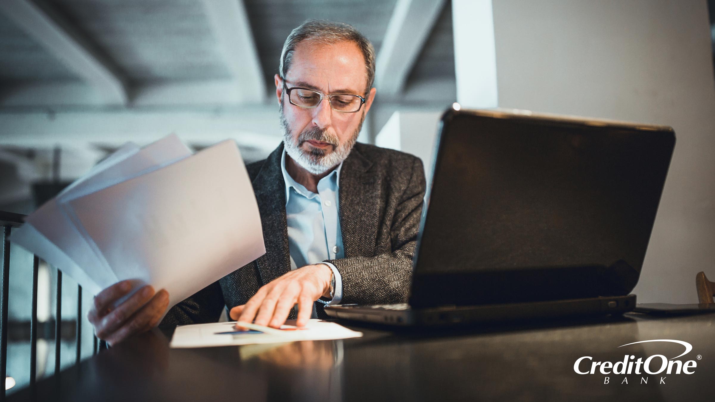 A mature man sits at his laptop sorting through documents and preparing for what will happen to his debt when he dies.